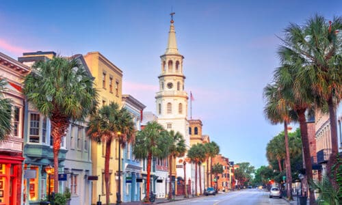 Brightly colored buildings with a white church steeple on a downtown street in Charleston, SC