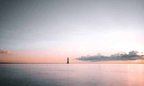 Long shot of the Morris Lighthouse shadowed in a soft peach sunset in Charleston, SC